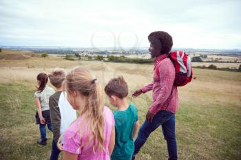 Adult Team Leader With Group Of Children At Outdoor Activity Camp Walking Through Countryside