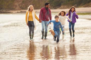 Multi-Cultural Family With Pet Dog Walking Along Beach Shoreline On Winter Vacation