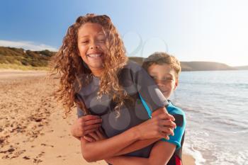 Portrait Of Two Children Wearing Wetsuits Standing By Waves On Summer Beach Vacation
