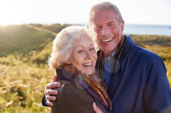 Portrait Of Loving Active Senior Couple Walking Along Coastal Path In Autumn Together