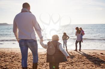 Rear View Of Family Walking Towards Sea Silhouetted Against Sun