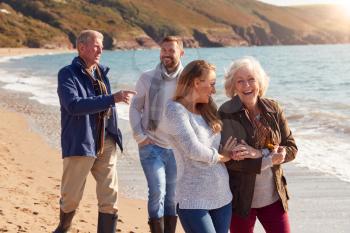 Senior Couple Walking Along Shoreline With Adult Offspring On Winter Beach Vacation