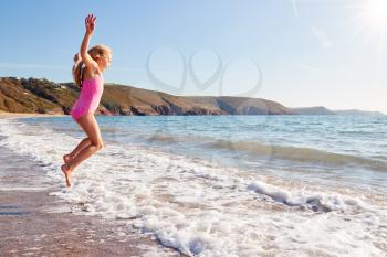 Girl Wearing Swimming Costume Having Fun Jumping Over Waves On Beach On Summer Vacation