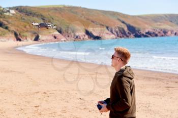 Young Man Flying Drone With Camera On Beach With Waves In Background