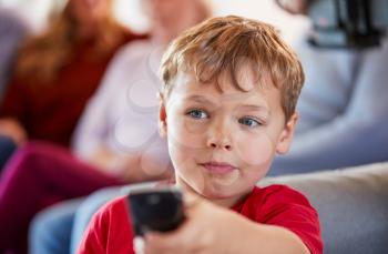 Boy Watching Television At Home With Multi-Generation Family Relaxing In Background