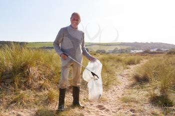 Portrait Of Senior Man Collecting Litter On Winter Beach Clean Up