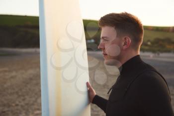 Young Man Wearing Wetsuit Enjoying Surfing Staycation On Beach As Sun Sets