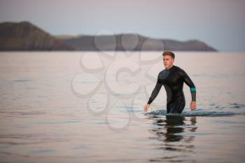 Man Wearing Wetsuit Wading Through Shallow Sea By Shore