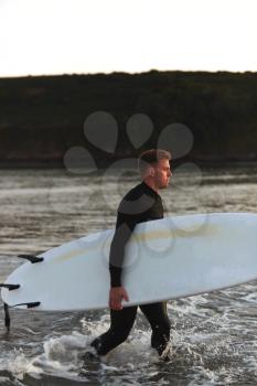 Man Wearing Wetsuit Carrying Surfboard As He Walks Out Of Sea