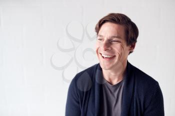 Portrait Of Casually Dressed Smiling Man Standing Against White Studio Wall