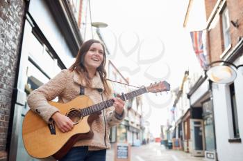 Female Musician Busking Playing Acoustic Guitar Outdoors In Street