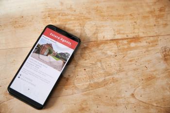 Close Up Of Mobile Phone With Realtors Property App Lying On Table