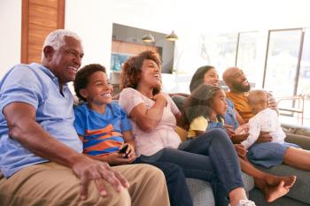 Multi-Generation African American Family Relaxing At Home Sitting On Sofa Watching TV Together