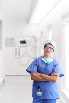 Portrait Of Young Male Doctor Wearing Scrubs Standing In Hospital Corridor