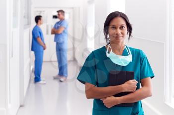 Portrait Of Smiling Female Doctor Wearing Scrubs In Hospital Corridor Holding Digital Tablet