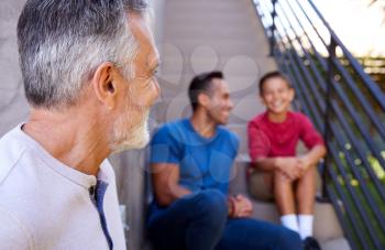 Smiling Multi-Generation Male Hispanic Family Sitting On Steps In Garden And Talking Together