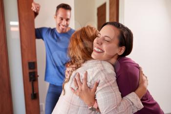 Couple Greeting Senior Father At Front Door As He Comes To Visit