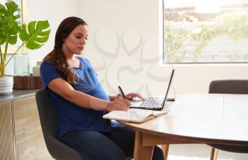Pregnant Woman Using Laptop At Table Working From Home