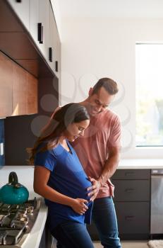 Loving Hispanic Husband With Pregnant Wife At Home In Kitchen Together