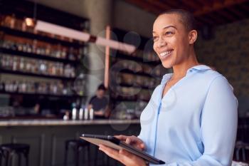 Confident Female Owner Of Restaurant Bar Standing By Counter Holding Digital Tablet