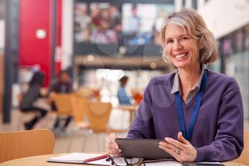 Portrait Of Mature Female Teacher Or Student With Digital Tablet Working At Table In College Hall