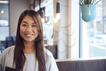 Head And Shoulders Portrait Of Smiling Young Asian Businesswoman  Working In Modern Office