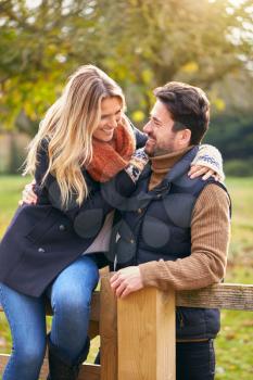 Loving Couple On Walk Through Autumn Countryside Sitting On Gate
