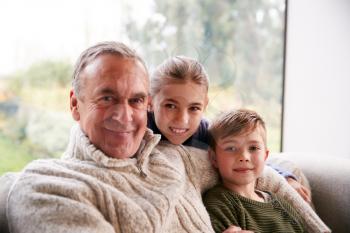 Portrait Of Grandchildren Sitting On Sofa At Home With Grandfather