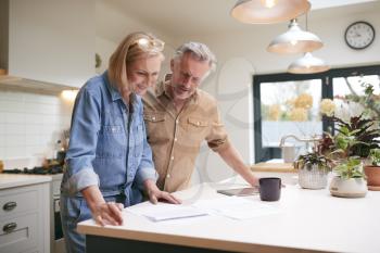 Mature Couple Reviewing Domestic Finances And Investments In Kitchen At Home Together