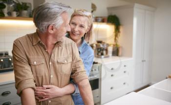 Loving Mature Couple Hugging As They Stand By Counter In Kitchen At Home