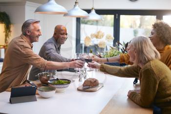 Group Of Mature Friends Making A Toast As They Meet At Home For Meal And Serve Food In Kitchen