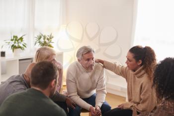 Group Consoling Man Speaking At Support Group Meeting For Mental Health Or Dependency Issues