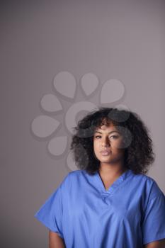 Studio Portrait Of Female Nurse Wearing Scrubs Standing Against Grey Background