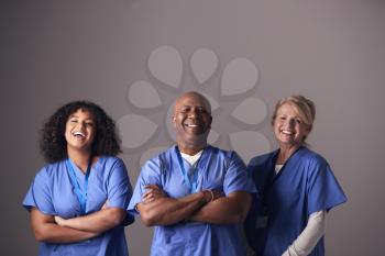 Studio Portrait Of Three Members Of Surgical Team Wearing Scrubs Standing Against Grey Background