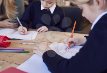 Close Up Of Mother Helping Son And Daughter Wearing School Uniform With Homework At Table In Kitchen