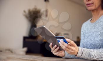 Close Up Of Mature Woman At Home Buying Products Online Using Digital Tablet And Credit Card