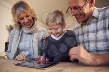 Grandson With Grandparents Playing On Digital Tablet At Home Together