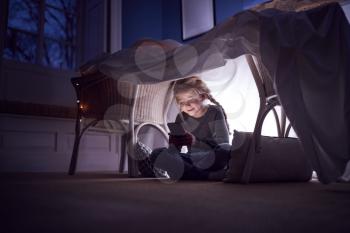 Girl Sitting In Den Or Camp She Has Made At Home Playing With Mobile Phone