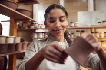 Female Potter Fitting Clay Handles To Mugs In Ceramics Studio