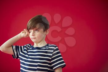 Portrait Of Tired Boy Rubbing Eyes Against Red Studio Background
