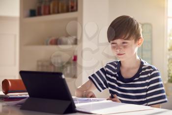 Boy Sitting At Kitchen Counter Doing Homework Using Digital Tablet