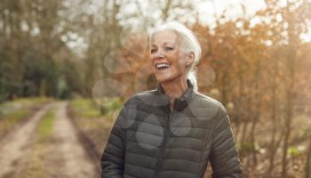 Smiling Senior Woman On Walk In Autumn Countryside Exercising During Covid 19 Lockdown