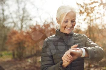 Senior Woman Running In Autumn Countryside Exercising Checking Smart Watch Fitness Activity App