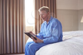 Bereaved Senior Man Sitting On Edge Of Bed Looking At Photo In Frame