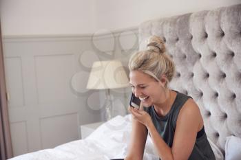 Businesswoman Sitting On Bed With Mobile Phone Working From Home During Pandemic Lockdown