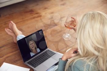 Woman Having Video Chat With Friend Sitting On Floor At Home Relaxing With Wine