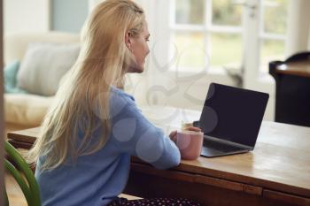 Rear View Of Woman Sitting At Table With Laptop Having Video Chat With Friend At Home