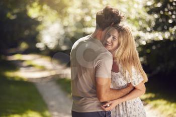 Loving Couple Hugging As They Walk Along Countryside Path In Summer Together