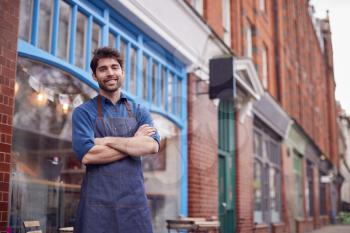 Portrait Of Male Small Business Owner Wearing Apron Standing Outside Shop On Local High Street
