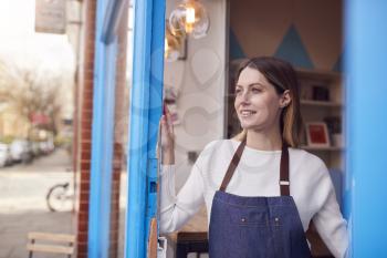 Smiling Female Small Business Owner Standing In Shop Doorway On Local High Street